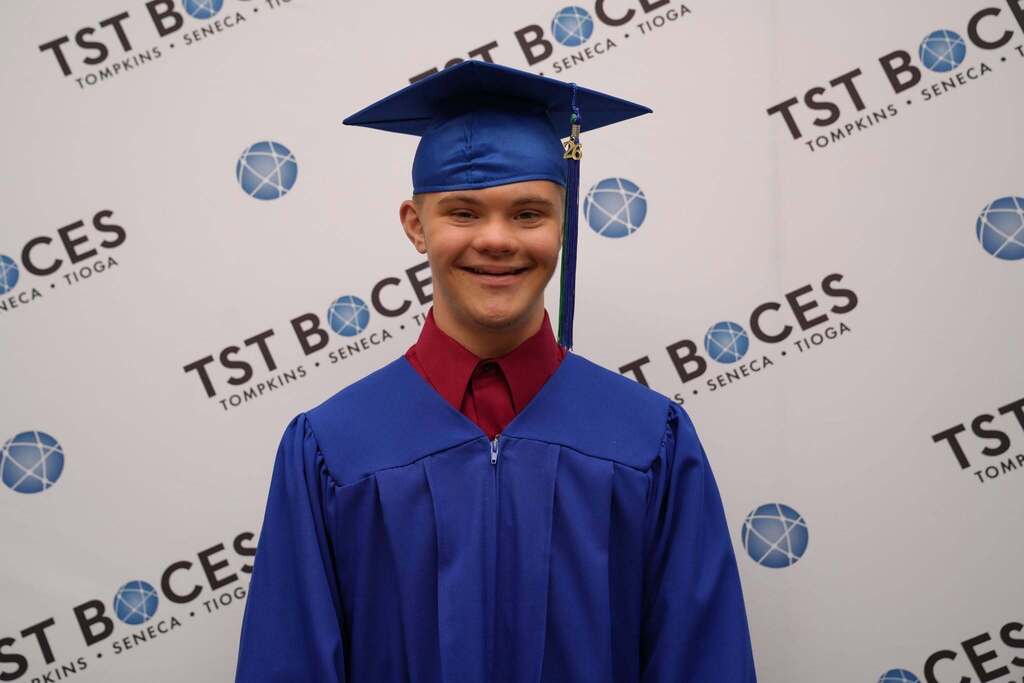 Graduate poses in front of a TST BOCES graduation backdrop