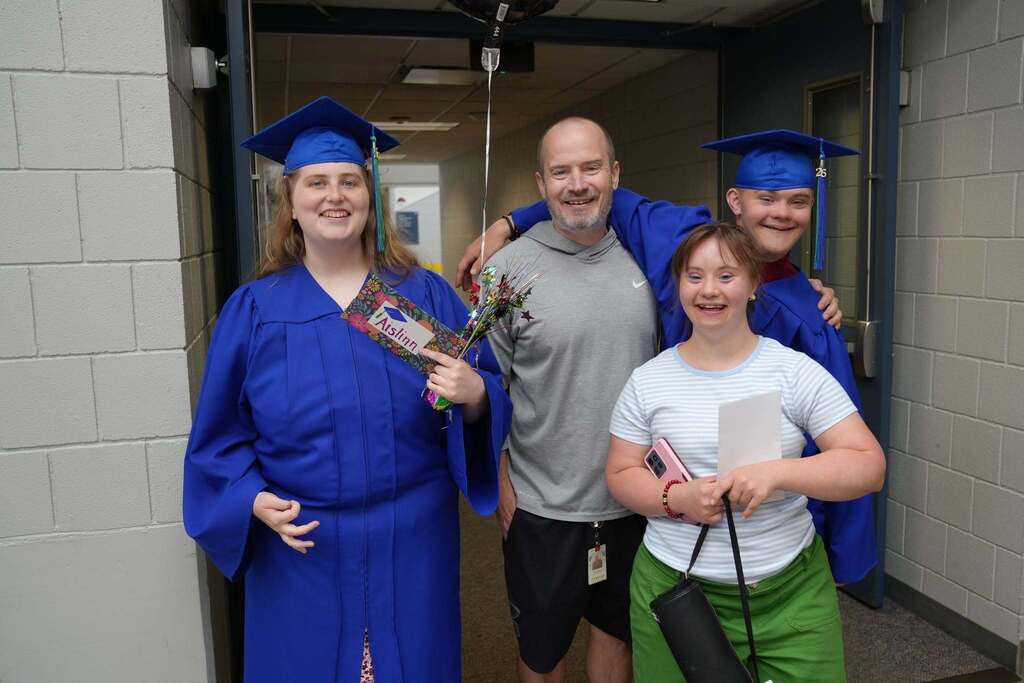 Graduates pose with a staff member and a family member after the gradaution ceremony comenses and smiles at camera for a picture