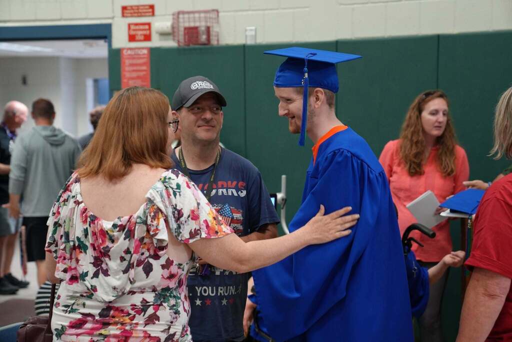 Graduate in a blue cap and gown speaks with family members and guests following the graduation ceremony.