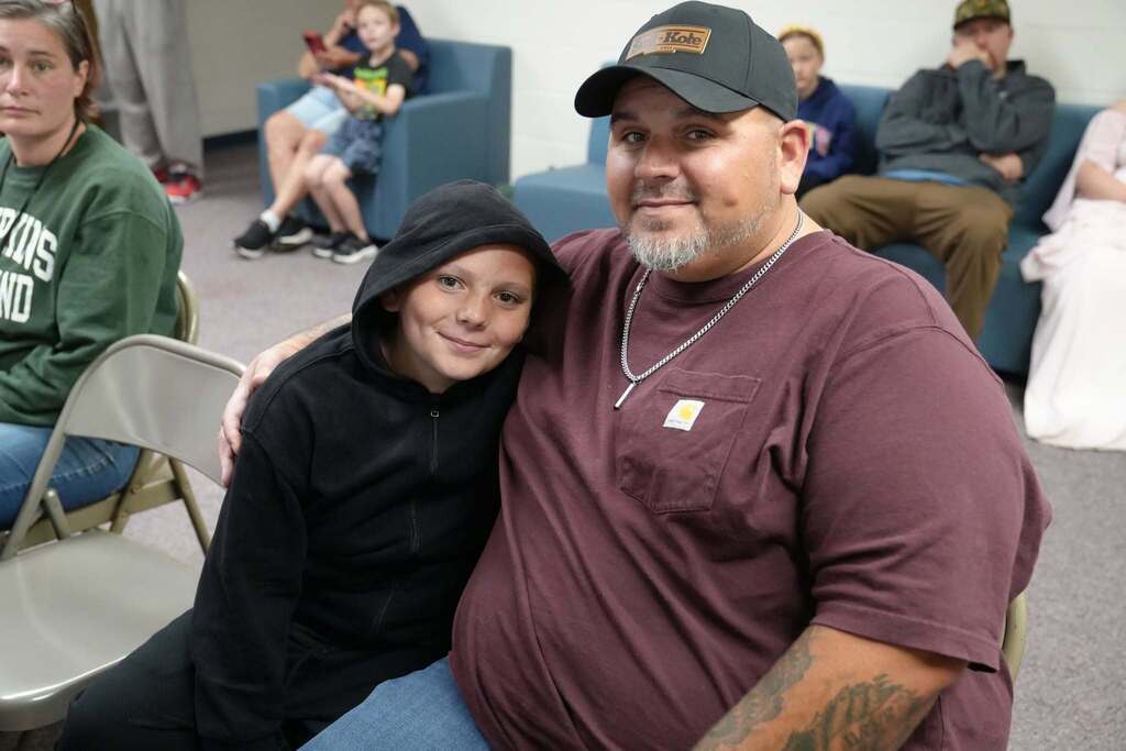 A student sits with a family member during the Turning Point Elementary awards ceremony, smiling together while waiting for the celebration to begin.