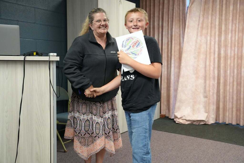 A student smiles while shaking hands with a staff member after receiving a personalized word art print during the Turning Point Elementary awards ceremony.