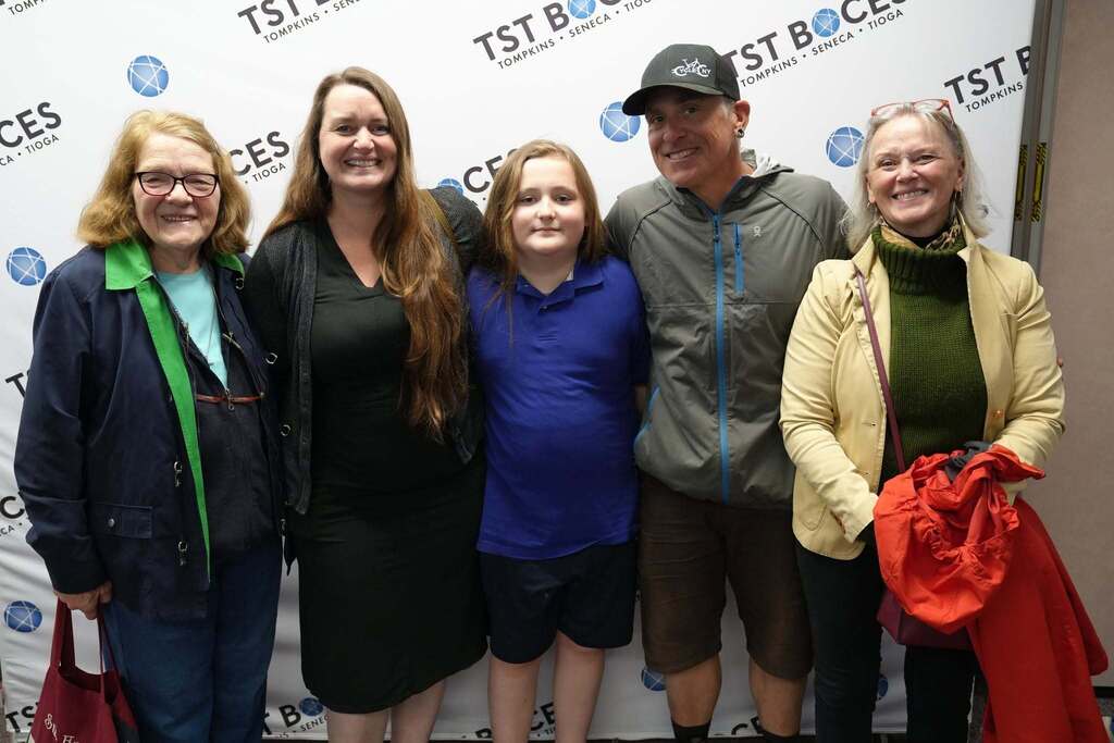 A Turning Point Elementary student smiles while posing with four family members in front of a TST BOCES backdrop after the end-of-year awards celebration.