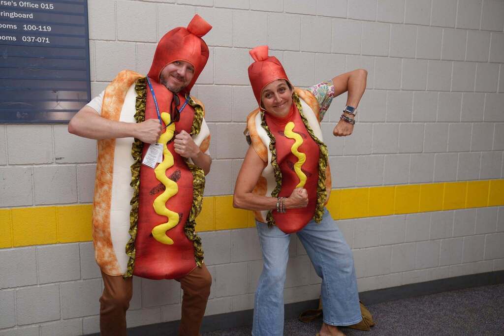 Two TST BOCES staff members pose in matching hot dog costumes, flexing their arms and smiling for the camera during the Annual Hot Dog Day celebration.