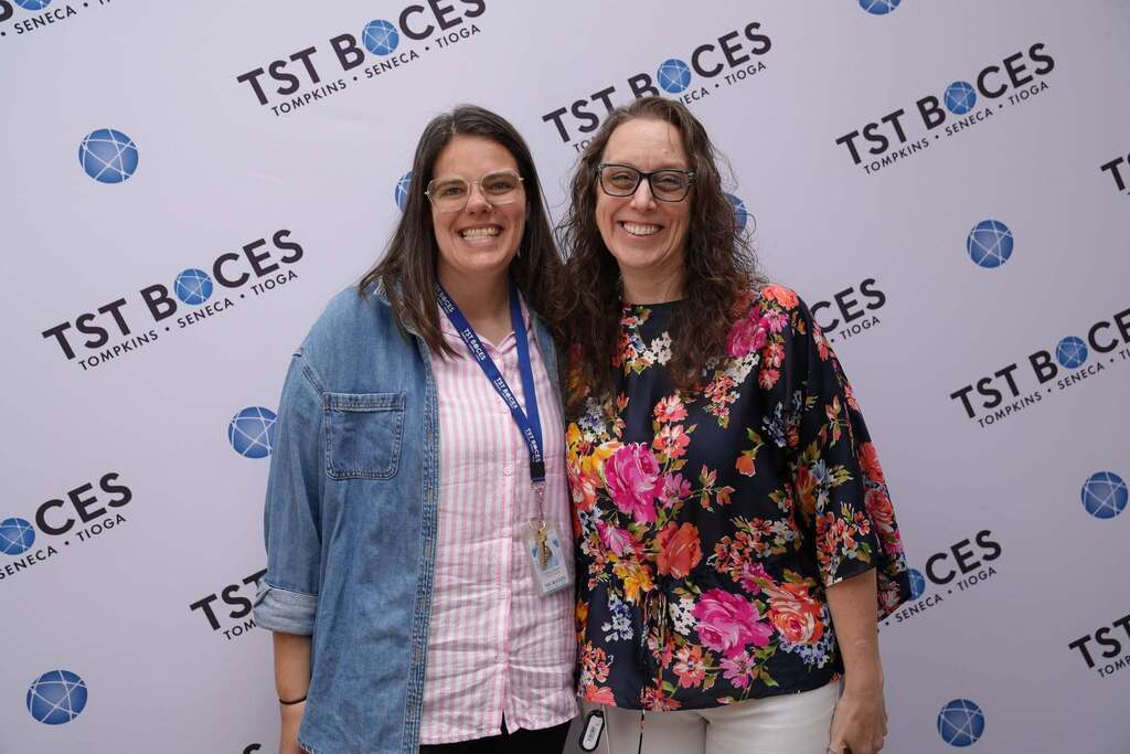 Two TST BOCES staff members smile together in front of a TST BOCES backdrop during the Annual Hot Dog Day celebration.