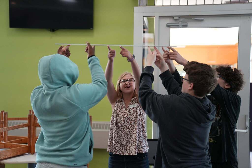 A group of incoming P-TECH students work together to balance a long rod using only their fingertips during a Bridge Week team-building challenge.