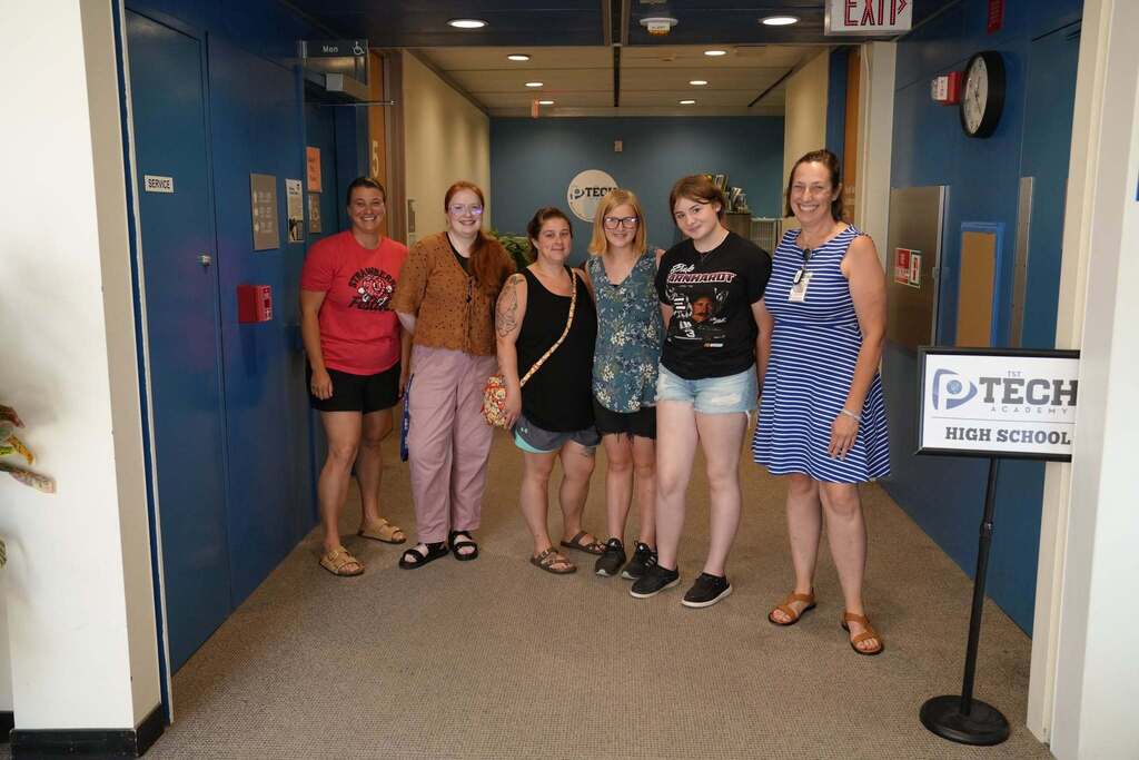 Incoming P-TECH students, family members, and staff pose together in the hallway outside the P-TECH Academy entrance during Bridge Week.