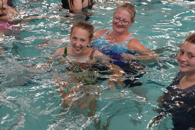 A student smiles while swimming alongside a staff member in the TC3 pool during a summer school field trip.