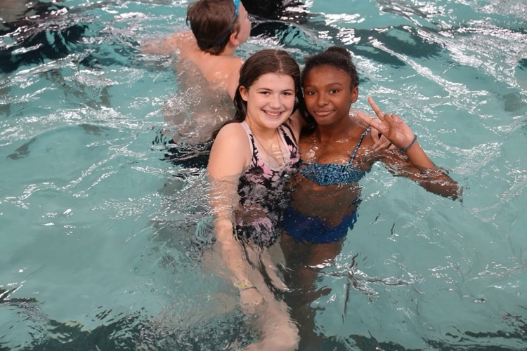 Two students smile for the camera in the pool, with one making a peace sign during a summer school swim outing at TC3.