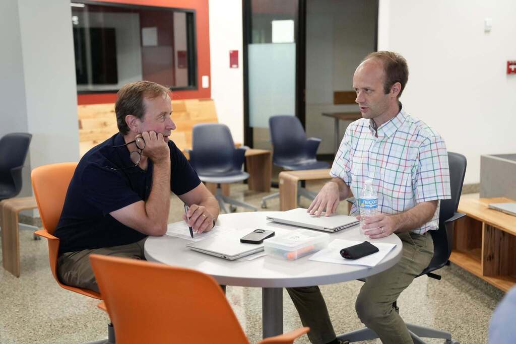 Two educational leaders meet at a table with laptops and notes, discussing ideas during a collaborative work session.