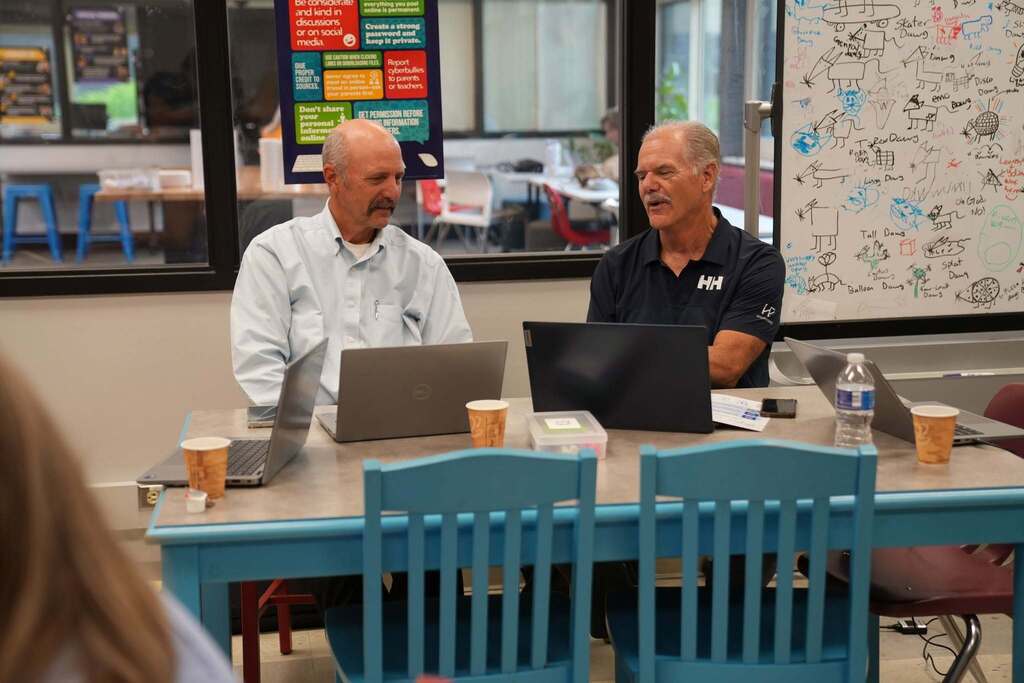 Two administrators sit together with laptops, discussing ideas during a hands-on AI breakout session.