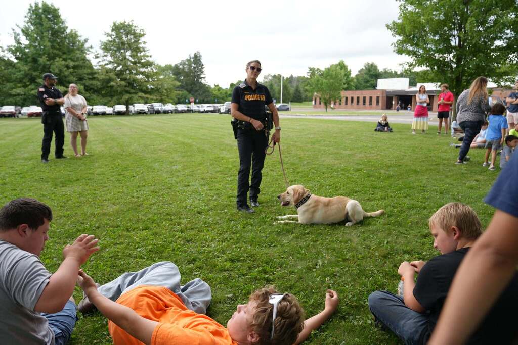 Investigator Melissa Sholar of Cortland University Police stands with K-9 Meekah, a yellow Labrador retriever, while students sit on the grass watching a K-9 demonstration.