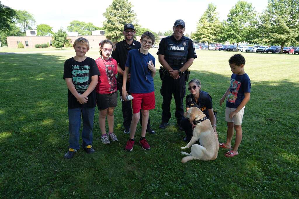 Students pose for a group photo with Sgt. Coakley, Sgt. Hollenback, Investigator Melissa Sholar, and K-9 Meekah, a yellow Labrador retriever, following a K-9 demonstration.