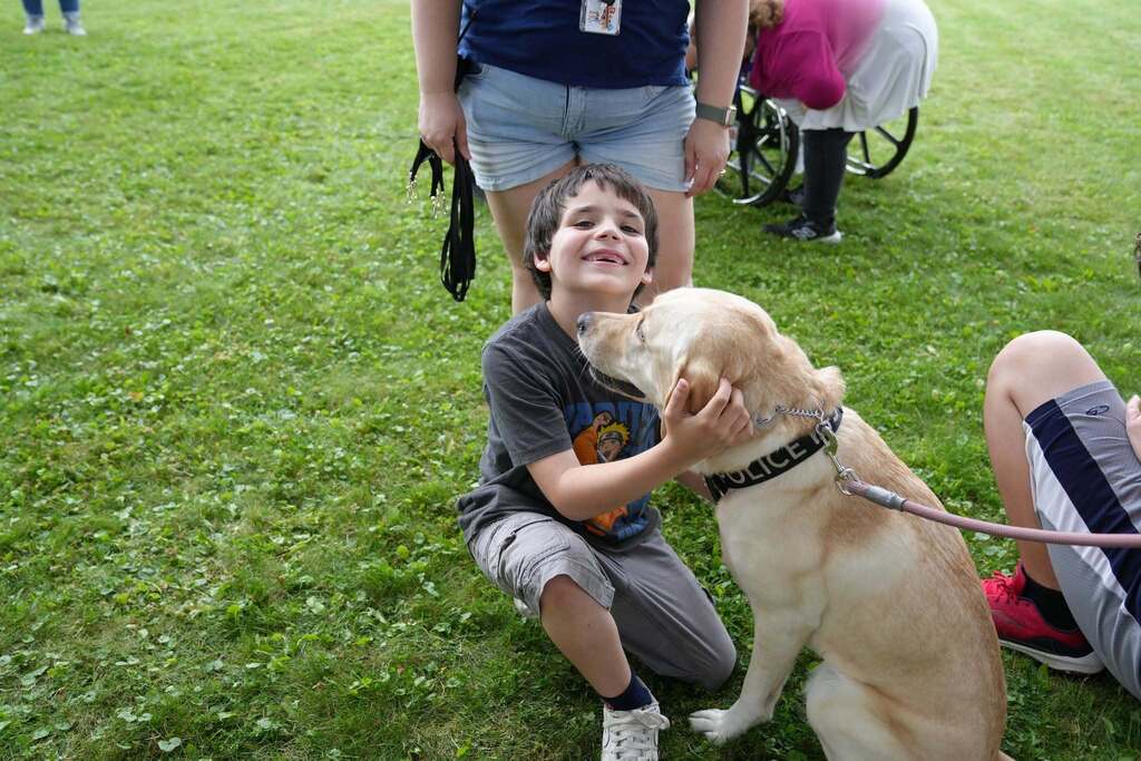 A smiling student hugs K-9 Meekah, a yellow Labrador retriever from Cortland University Police, while classmates and staff gather nearby after the K-9 demonstration.