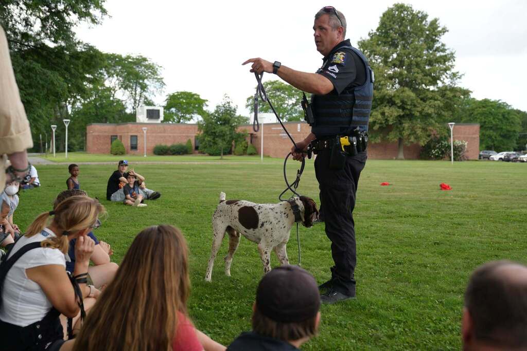 Sgt. Coakley of Cortland University Police speaks to students while standing with K-9 Red, a white and brown German Shorthaired Pointer, during an outdoor K-9 presentation.