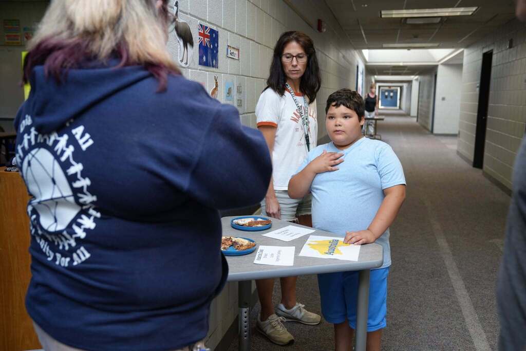 A Summer School student stands behind a table displaying food representing Australia while a staff member stands beside him during the World Cup Flavor event.
