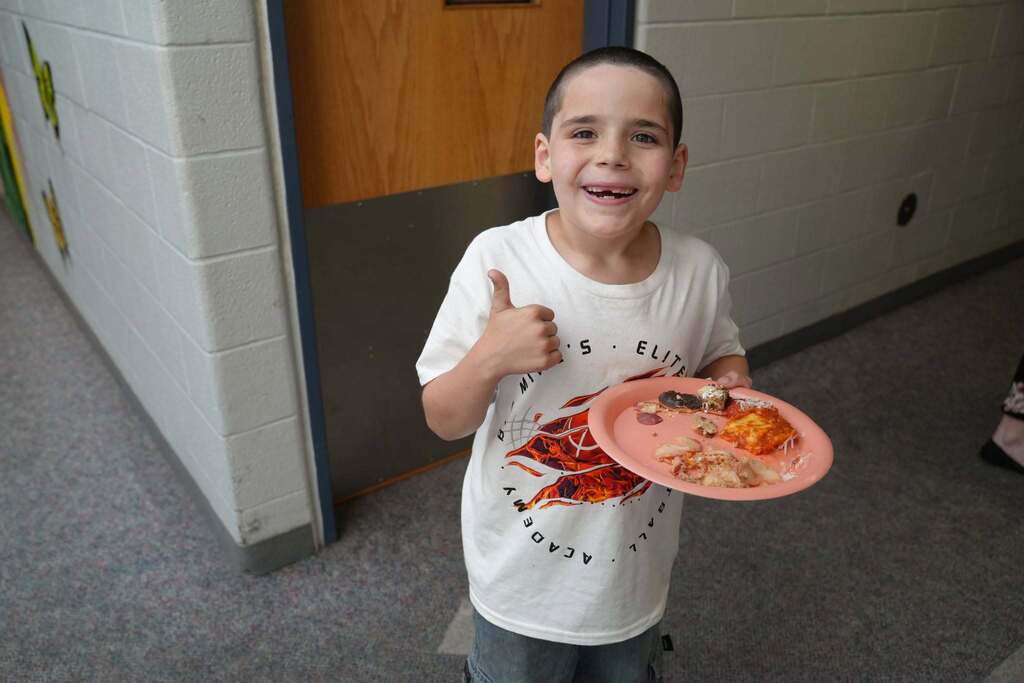 A smiling Summer School student gives a thumbs-up while holding a plate filled with samples from the World Cup Flavor event.