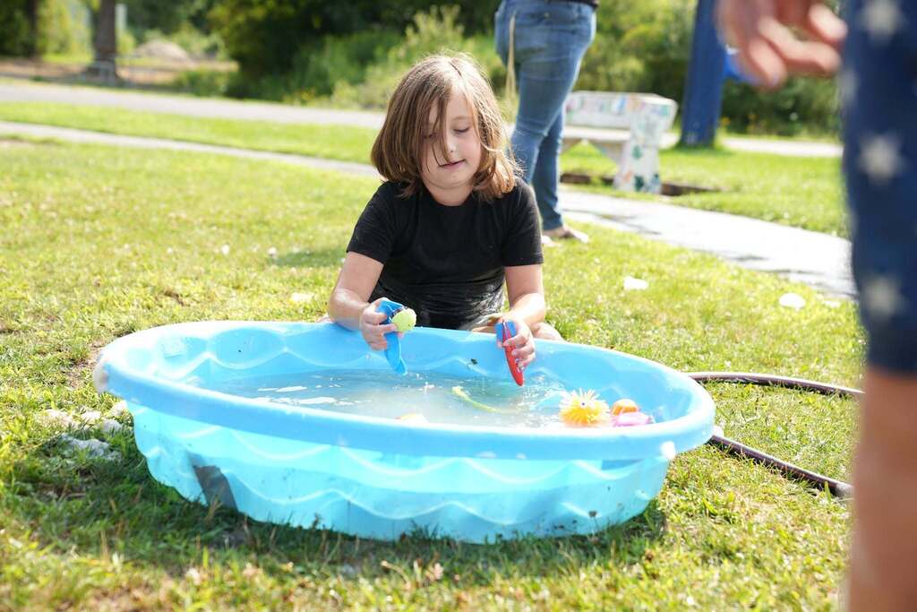 A Summer School student sits on the grass and plays with colorful sensory toys in a small blue pool filled with water during Water Play Day.