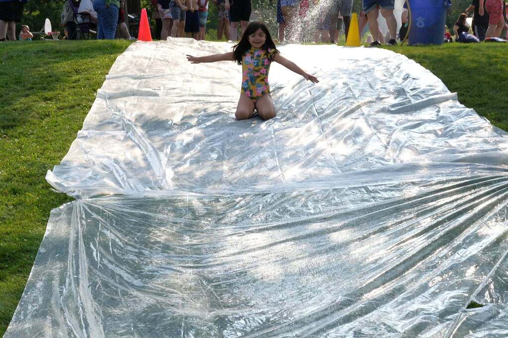 A young Summer School student slides down a large water-covered slip and slide with her arms stretched out during Water Play Day.