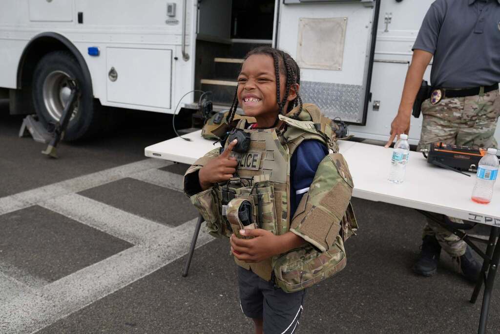 A smiling student tries on an oversized police tactical vest while learning about law enforcement equipment during Community Day.