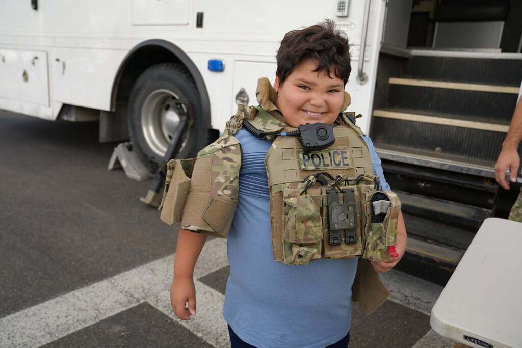 A smiling student wears an oversized police tactical vest while learning about the specialized equipment officers use.