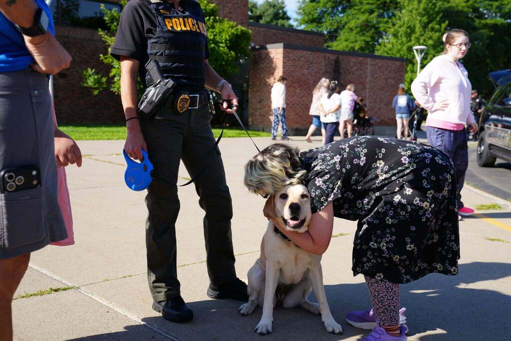 A student hugs a police K-9 while an officer holds the dog’s leash during TST BOCES Summer School Community Day.