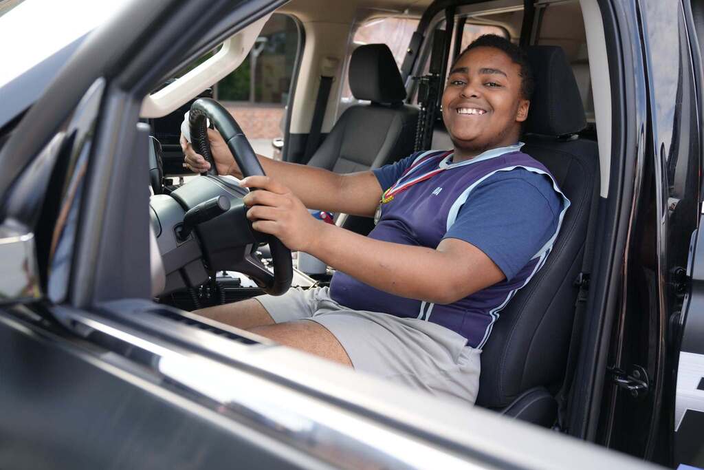 A student smiles while sitting behind the wheel of a police vehicle during TST BOCES Summer School Community Day.