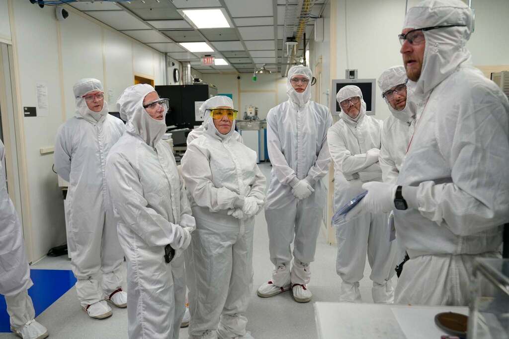 NYSED, TST BOCES, and local politicians wearing full cleanroom suits and safety glasses listens as a Cornell NanoScale Science and Technology Facility staff member explains equipment during a tour.