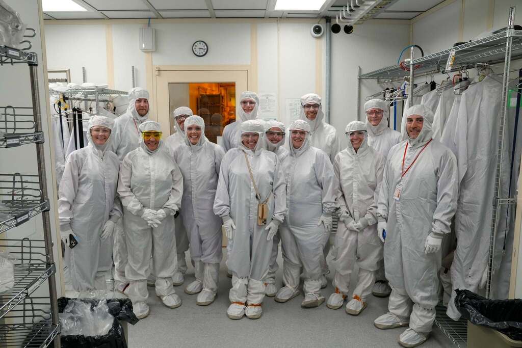 A large group of visitors poses together in cleanroom suits before touring the Cornell NanoScale Science and Technology Facility.