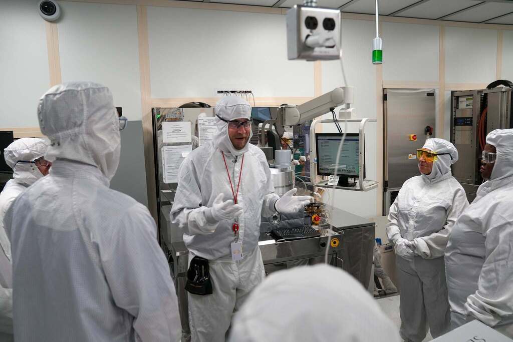 NYSED, TST BOCES, and local politicians wearing full cleanroom suits and safety glasses listens as a Cornell NanoScale Science and Technology Facility staff member explains equipment during a tour.
