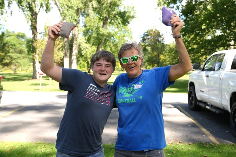 An RAS student and staff member celebrate their teamwork, smiling and holding up beanbags, illustrating the friendly cornhole matches at the annual picnic. 