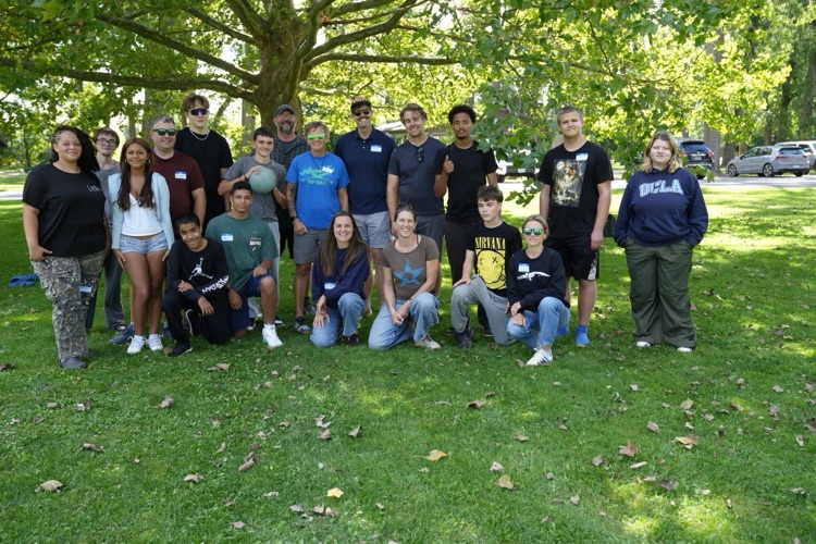 A large group of RAS students and staff smiling and posing together under a tree, representing the community coming together for the annual picnic at Myers Park to start the school year.