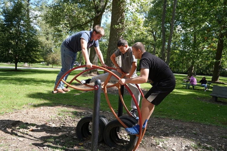 Three teenage boys challenge themselves on a unique arch-shaped climbing structure at the park playground, collaborating and having fun outdoors.