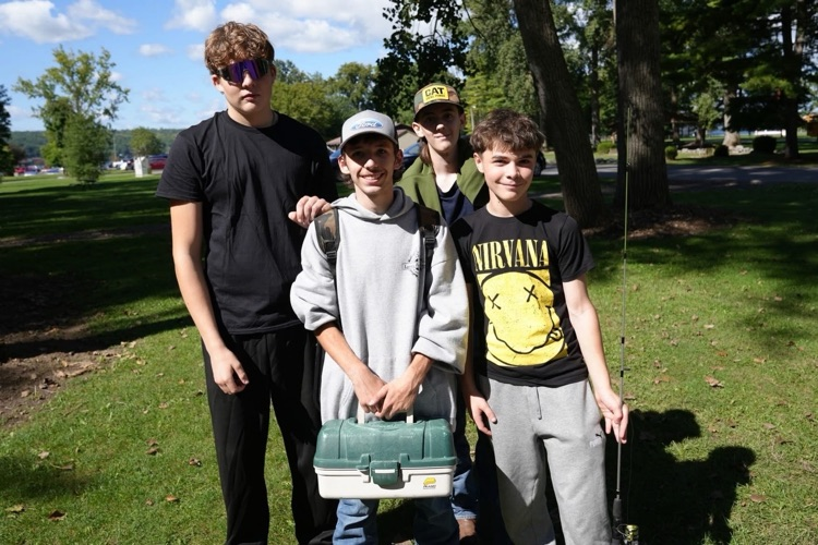four teenage boys smile at the camera while holding a tackle box and fishing pole