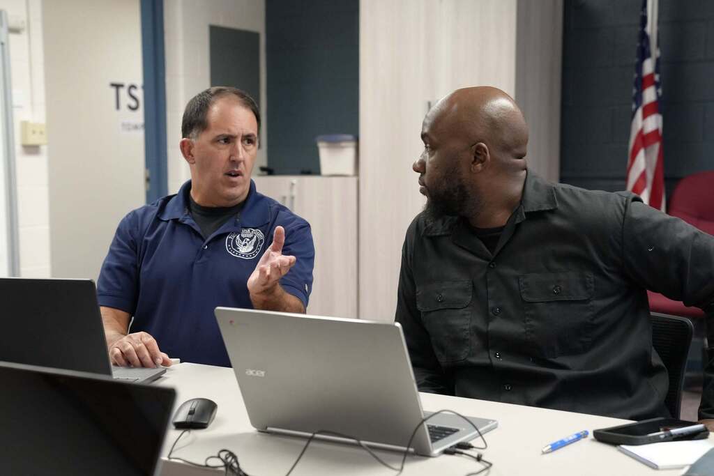A tompkins county member talks with a hiring event applicant across a table with laptops as they work through the application process.