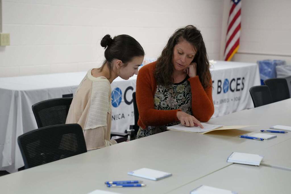 A staff member reviews application paperwork with a prospective employee seated at a table during the TST BOCES Hiring Event.
