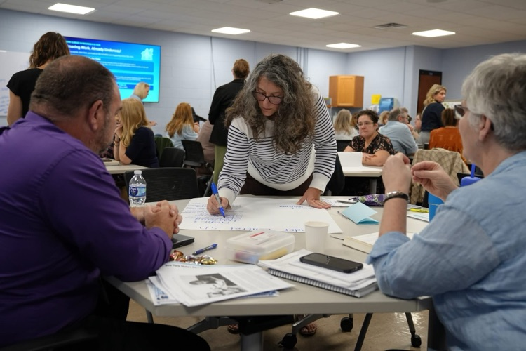 An educator standing over a table to write notes on large chart paper during a small group brainstorming activity.