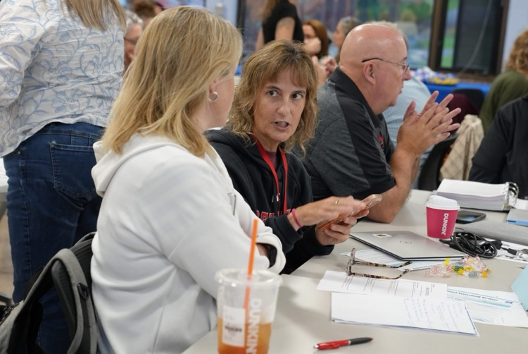Two educators sitting at a table with drinks and workshop materials, engaged in a discussion during the NY Transformation Coalition session.