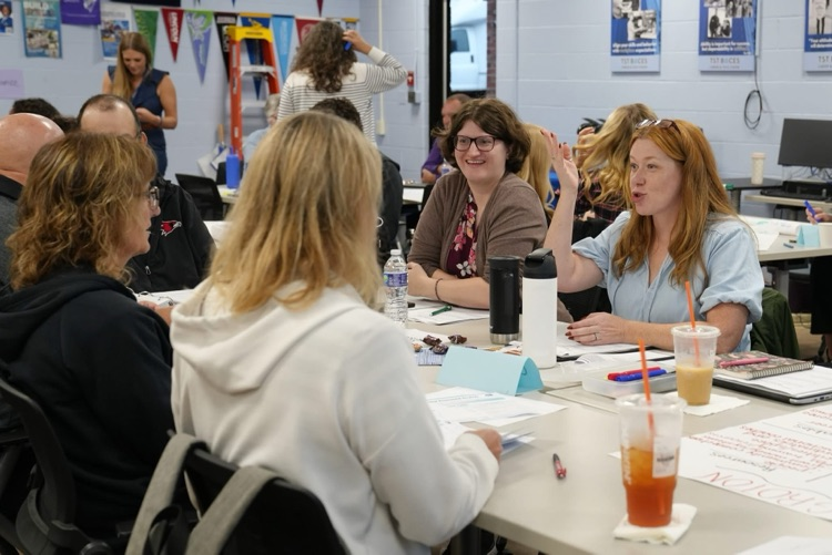 Educators seated at a workshop table sharing ideas, with one woman gesturing while speaking to her colleagues.