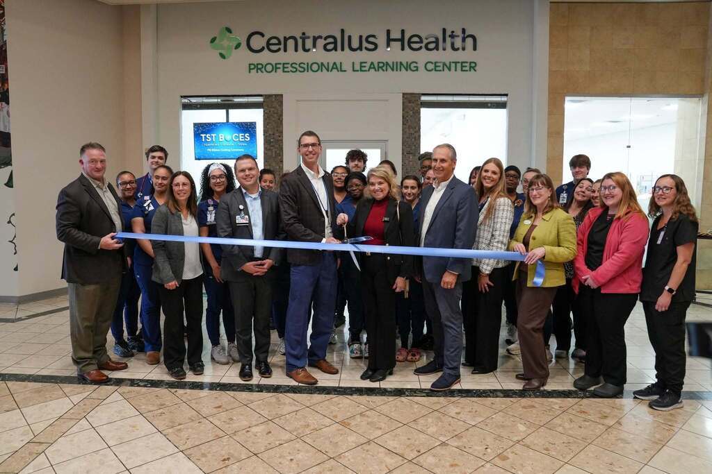 A large group of TST BOCES and Centralus Health staff along with Practical Nursing students in scrubs gather for a ribbon cutting. In the center, Dr. Berlin and Cindy Walter cut a blue ceremonial ribbon. Signage above reads Centralus Health Professional Learning Center