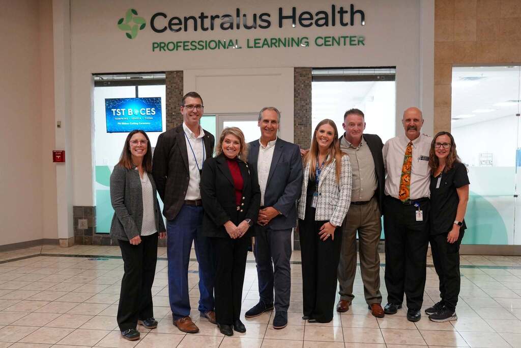 A group of eight community leaders, educators, and staff pose together under the Centralus Health Professional Learning Center sign. They are standing in the mall foyer following the ribbon cutting.