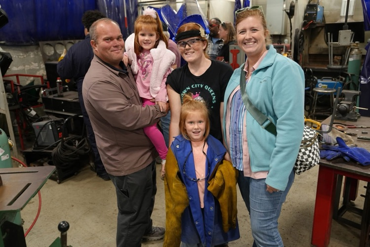 Family of five smiles at camera in welding classroom at Open House