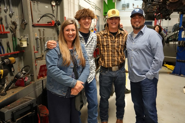family of four smiles to camera in auto tech classroom at open house
