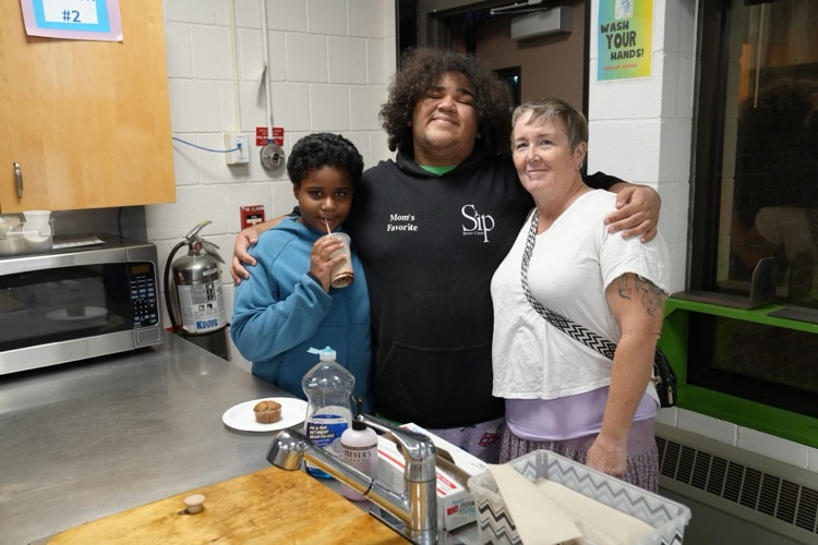 family of three stands with arms wrapped around each other in food service classroom at open house
