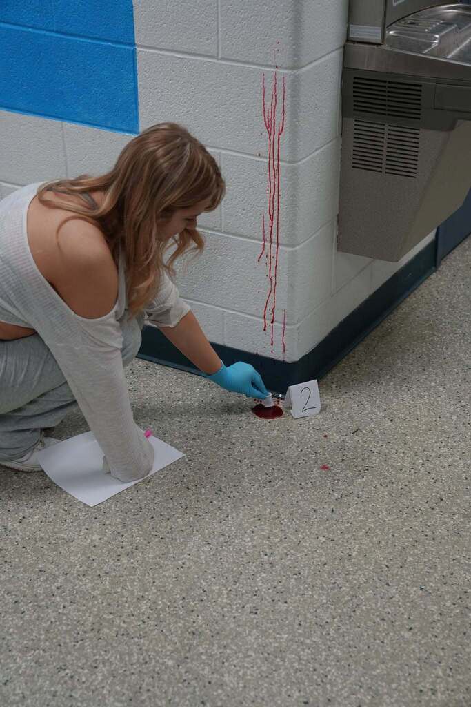 student bends down to collect a faux blood sample for CSI forensics lab