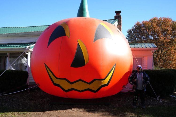 one student stands next to a large pumpkin inflatable