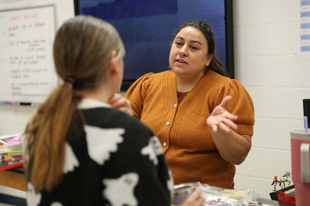 Two educators engage in a focal one-on-one conversation, with one woman gesturing expressively while speaking to a colleague in a ghost-patterned sweater.