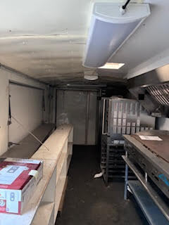 Interior view of the food trailer showing long service counters, overhead lighting, commercial cooking equipment, and a spacious work area.