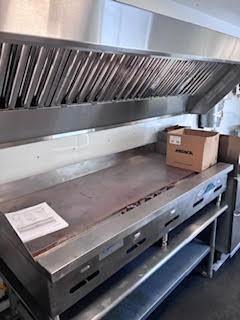Stainless steel flat top grill with large commercial ventilation hood above, included with the food trailer.