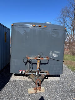 Front view of the dark gray food trailer showing the hitch assembly and enclosed trailer body parked on a gravel surface.