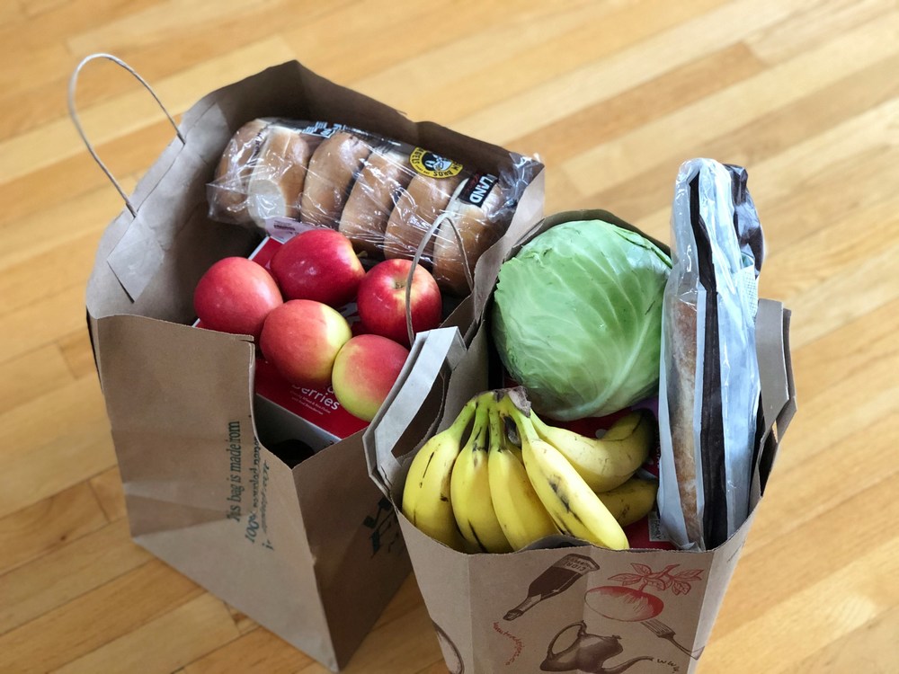 bags of groceries with vegetables and bagels in brown paper bags on a floor